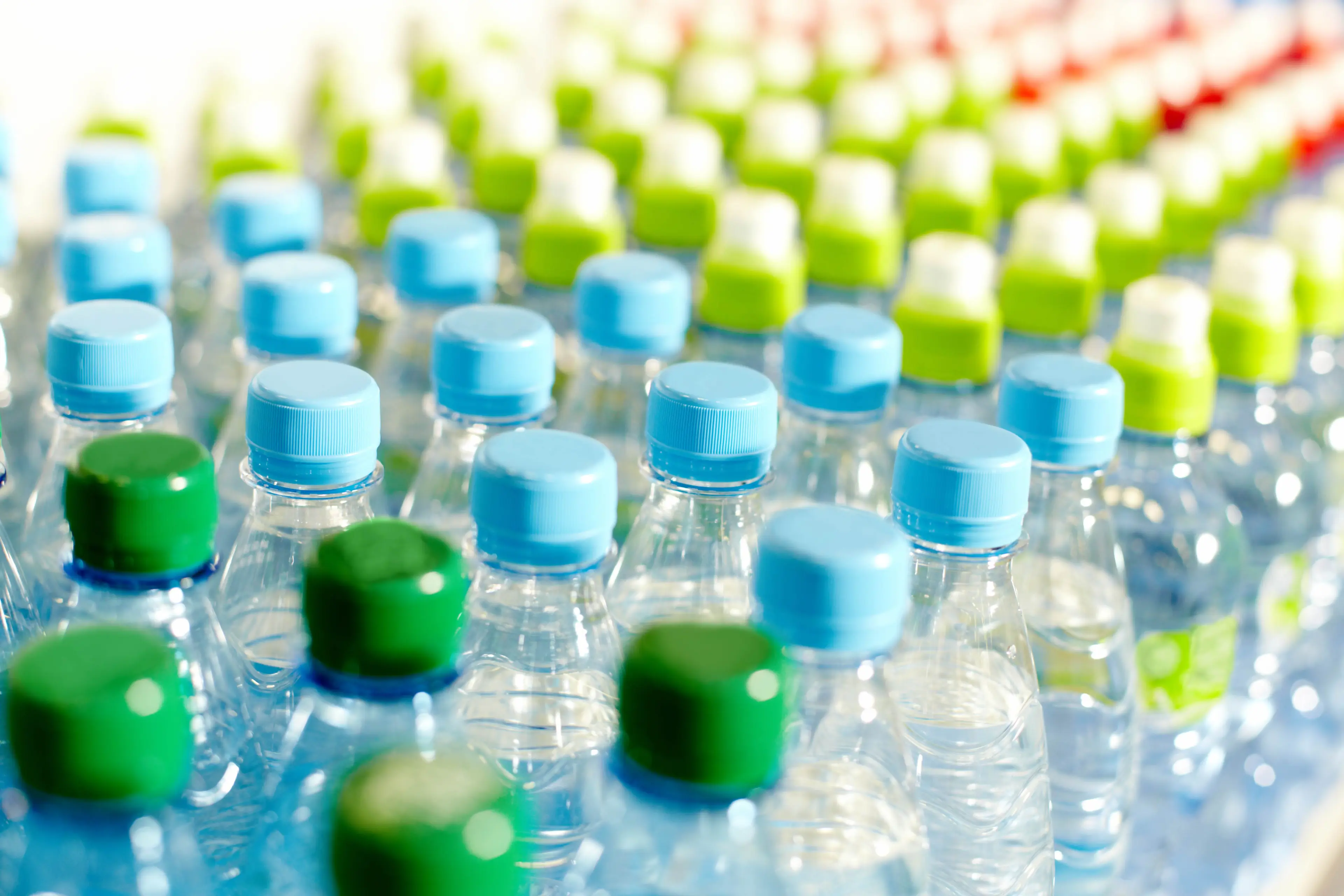 Many rows of plastic bottles with colorful tops lined up in an organized manner.