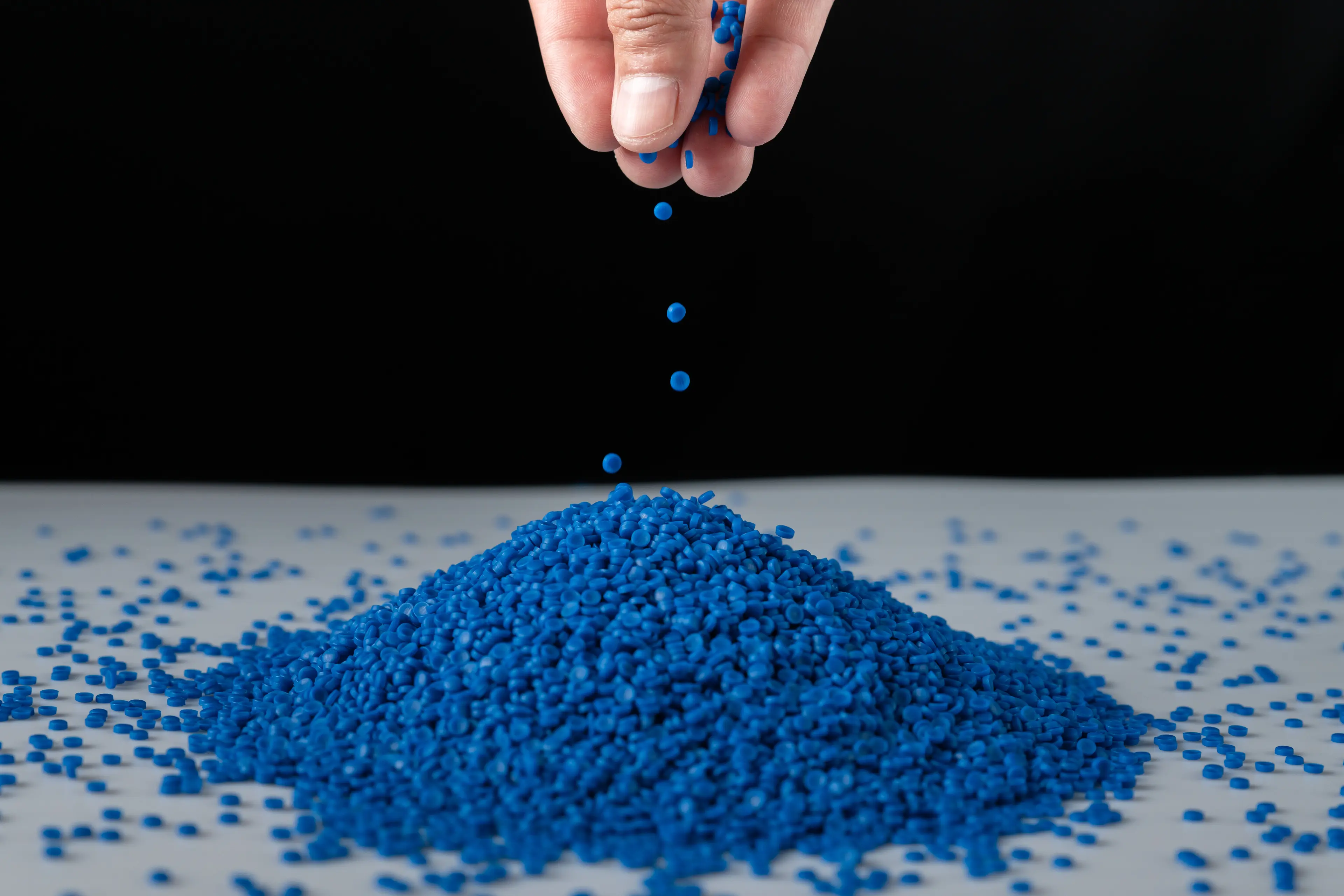 Hand sprinkling blue polypropylene pellets on white surface with black background