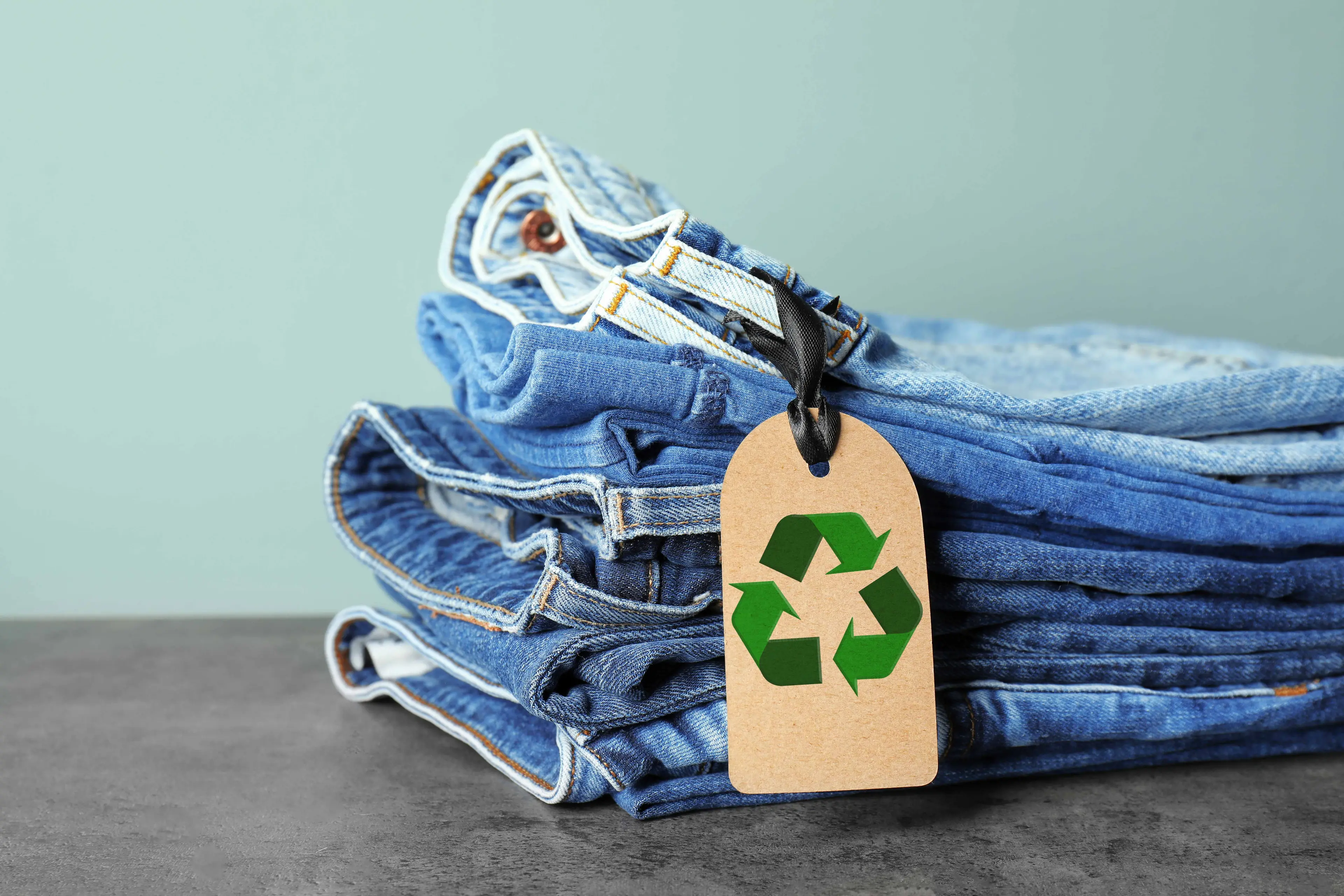 Pile of Jeans with recycled label attached on wooden table